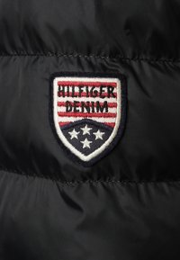 Black puffer fabric featuring an embroidered shield logo with red and white stripes, and five stars in a blue section.