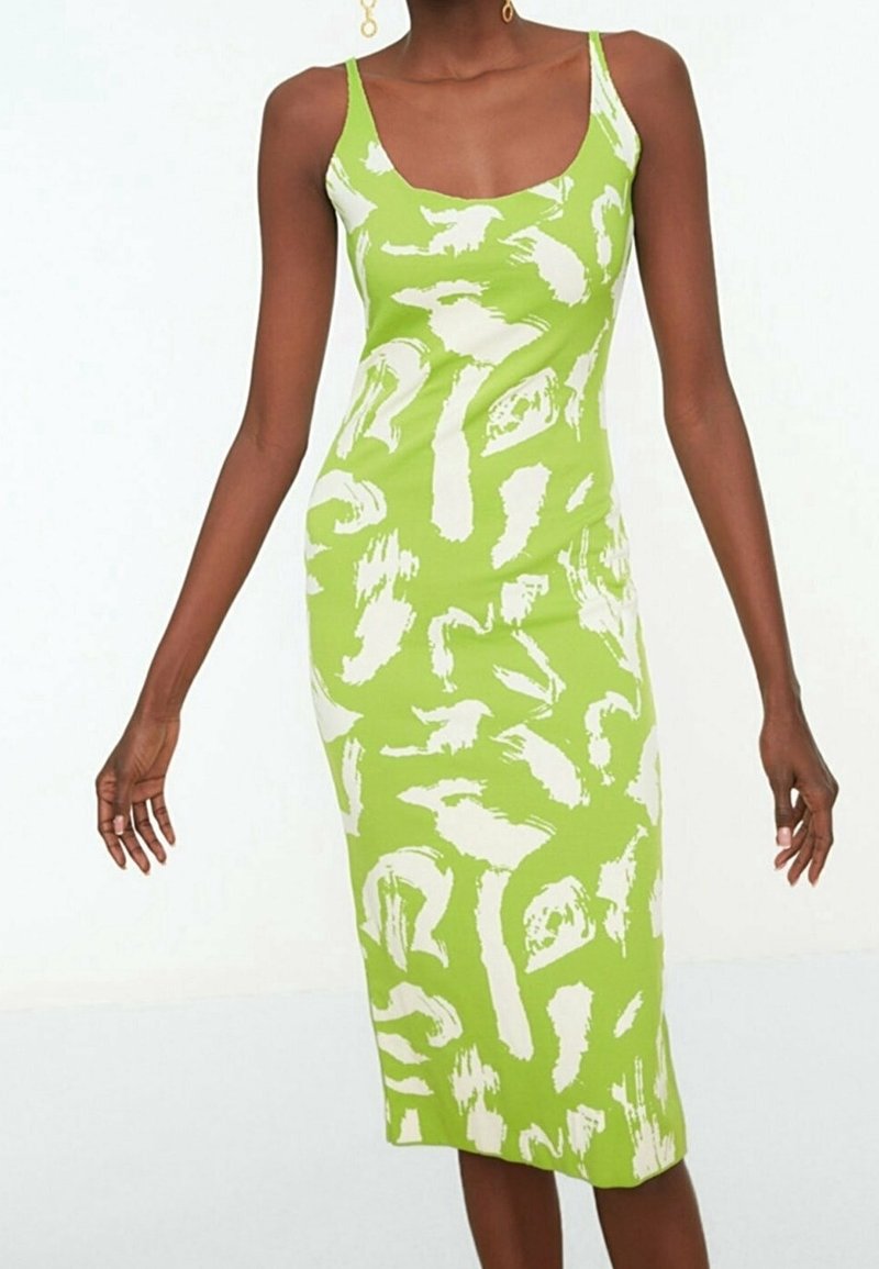 Femme portant une robe midi sans manches, ajustée, avec un imprimé abstrait vert et blanc et un col en amande.