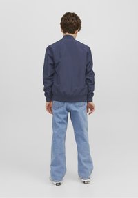 Granatowa kurtka bombowiec z prążkowanym kołnierzem i mankietami, w połączeniu z jasnoniebieskimi spodniami typu wide-leg. Materiał wydaje się gładki o matowym wykończeniu.