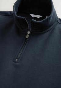Marineblauwe pullover met een hoge kraag en een kwart ritssluiting. Gemaakt van zachte stof, met een gladde textuur en een minimalistisch ontwerp.