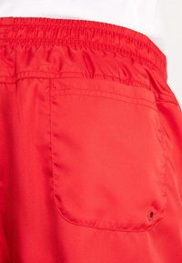 Röda shorts gjorda av mjukt, lättviktigt tyg, med en elastisk midja och en bakficka med en synlig knappdetalj.