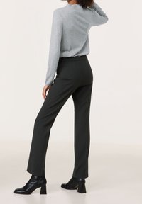 Šedý dlouhý rukáv, černé kalhoty na míru a černé boty na podpatku za kotníky. Hladké textury a přiléhavý střih. Minimalistický design.
