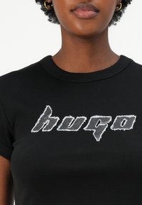 Černé tričko s krátkým rukávem, které na přední straně zdobí distressed šedé logo "hugo". Vyrobeno z hladké tkaniny, má fitted design a žebrovaný límec.
