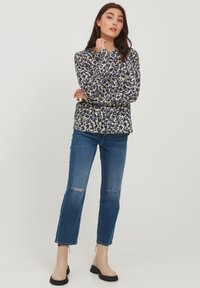 Beige- und blaue Leopardenmuster Langarmoberteil, kombiniert mit ausgewaschenen blauen Jeans und beige Ankle Boots mit schwarzen Sohlen.
