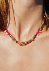 Collier doré mettant en valeur des perles roses, des accents turquoise et un ornement central orné d'une pierre bleue.