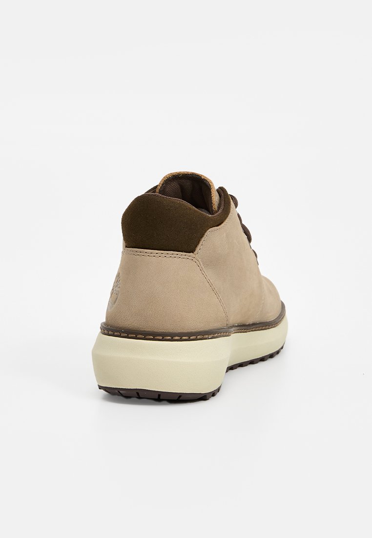 Zapato de ante beige con un cuello de ante marrón, punta redonda y una entresuela de color claro. Cuenta con una suela exterior de goma texturizada para mayor agarre.