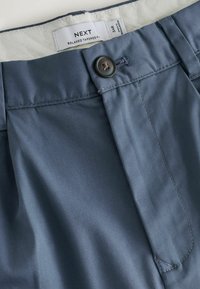 Pantaloni blu dal taglio aderente e rilassato con chiusura a bottone e etichetta interna visibile che indica la taglia 34R e il marchio NEXT.