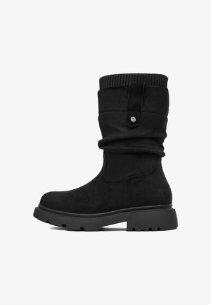 Czarny zamszowy but sięgający do połowy łydki, z prążkowanym mankietem, suwakiem, grubą, wytrzymałą podeszwą i zaokrąglonym noskiem, pokazany z boku, skierowany w lewo.