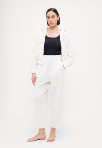Witte, gestructureerde hoodie met voorzakken, gecombineerd met bijpassende broek met elastische taille. Beide hebben een subtiel patroon en een relaxte fit.