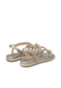 Sandali piatti realizzati in materiale metallicamente dorato, con un design di cinturino decorato di gioielli, texture liscia e suola imbottita per il comfort.
