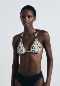 Trekantet bikinitopp i beige med svart leopardmønster, med halterneck-bånd. Kombinert med høyt midje svart bikini-bunn, myk tekstur.