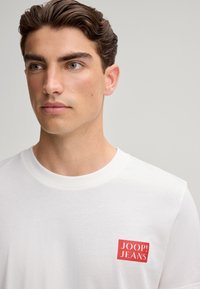 Biała bawełniana koszulka z okrągłym dekoltem i czerwonym prostokątnym logo na lewej piersi z napisem "JOOP! JEANS."