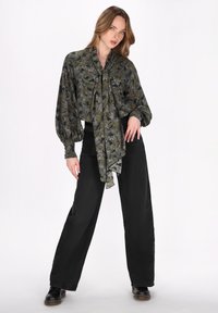 Bluză cu un model floral verde, cu un șnur la guler, combinată cu pantaloni negri cu croială largă și pantofi negri. Textură netedă, croială lejeră.