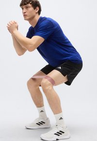 Atletska obleka z modro majico s kratkimi rokavi in črnimi kratkimi hlačami. Bela superga s črnimi poudarki. Elastični trak je nameščen okoli stegen.