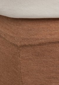 Bruine gebreide stof met een gladde textuur, met een elastische tailleband en een aansluitende pasvorm, gelaagd onder een wit topje.