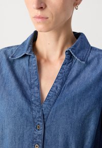 Denim srajca s ovratnikom, sprednjim gumbom in modrim tekstilom. Ima sproščen kroj in subtilne detajle šivanja.