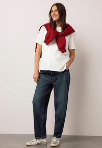 Tricou alb cu mâneci scurte, asortat cu blugi largi, de culoare albastru închis. Bluza roșie este legată în jurul umerilor. Adidași gri cu talpă alb-crem.