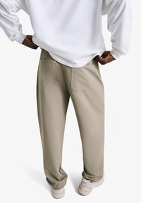 Bež sproščene hlače z dvema zadnjima žepoma, iz mehke tkanine. Nošene z belo majico z dolgimi rokavi in svetlimi supergami.