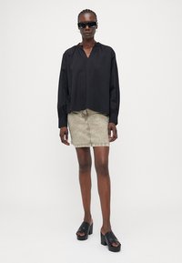 Black long-sleeve blouse with a v-neck, paired with a beige denim mini skirt and black platform mules. Accessories include black sunglasses.