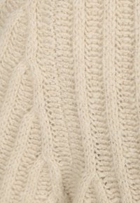 Crème gebreide trui met een textuur en ribpatroon. Beschikt over dikke garen met verschillende steken, wat diepte en visuele interesse creëert.