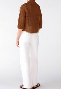 Hnědý pletený top s krátkými rukávy a volným střihem, doplněný bílými rovnými kalhotami a černými sandály. Top má strukturální vzor.