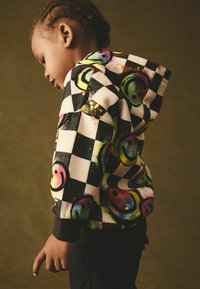 Hoodie z kapturem ma wzór w szachownicę z kolorowymi uśmiechniętymi buźkami. Wykonany z miękkiego materiału, ma ściągacze przy mankietach i luźny krój.