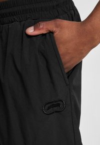 Schwarze Shorts mit einem elastischen Bund und seitlichen Taschen. Sie verfügen über einen strukturierten Stoff und ein gesticktes Logo-Patch auf dem Oberschenkel.