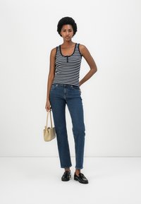 Camisola de tiras às riscas azul marinho e branca com um decote redondo, combinada com jeans de perna reta azul. Sapatos loafers pretos e uma pequena bolsa bege.