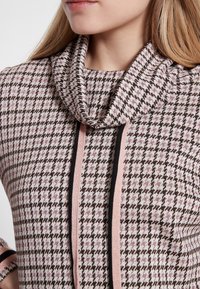 Pull à col châle en motif pied de poule rose et marron, avec des accents rayés noirs et roses sur le devant. Texture douce.