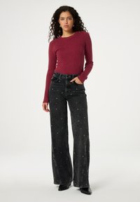 Langärmliges, geripptes bordeauxrot Oberteil, kombiniert mit weiten, hoch taillierten schwarzen Jeans mit silbernen Nietenakzenten.