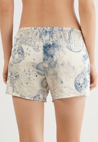 Pantalones cortos de estampado azul y crema con diseños celestiales, incluyendo planetas y estrellas, con una cinturilla elástica y una textura de tela suave.