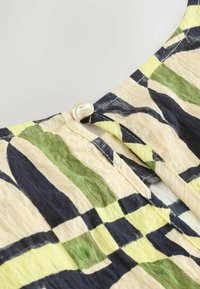 Tričko z potištěné látky s detailem u výstřihu, vzorovaným zelenou, námořnickou a žlutou mřížkou. Na zadní straně se nachází stříbrný ozdobný knoflík.
