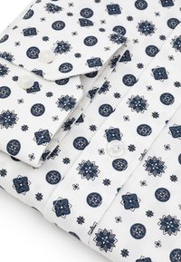 Biała koszula z powtarzającym się niebieskim wzorem kwiatowym i okrągłym. Dwa guziki widoczne na mankiecie, z gładką teksturą materiału.