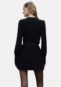 Vestito lungo nero con maniche lunghe, corpetto aderente, gonna plissettata e cintura legata in vita. Tessuto morbido e sottili dettagli di texture.