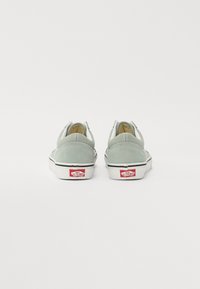 Zelene suede slip-on cipele s bijelom gumom, crnim trakama i crvenim logotipom na peti. Besprijekorni dizajn stražnjeg dijela.
