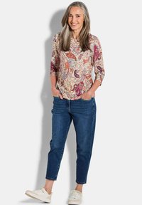 Bunt gemusterte Bluse mit Paisleymuster und 3/4-Ärmeln, kombiniert mit dunkelblauen schmal geschnittenen Jeans und weißen Sneakern.