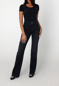 Czarna dopasowana bluzka z subtelnymi wzorami, połączona z czarnymi dżinsami z wysokim stanem i dzwonami. Czarne czółenka z dekoracyjnymi akcentami.