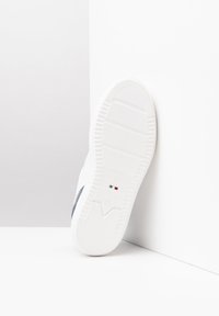 Baskets blanches avec une semelle texturée, présentant une accent bleu marine et une marque italienne. Le design est minimaliste avec une finition lisse.