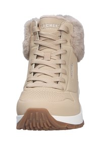 Zapatilla deportiva de caña alta color beige con cuello de piel sintética, parte superior texturizada, diseño de cordones y suela de goma con un diseño de agarre pronunciado.