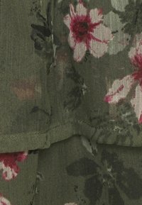 Tela con estampado floral en verde con flores rosas y blancas. Presenta un dobladillo en capas y una textura suave.