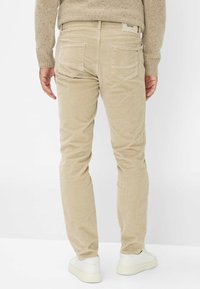Beige corduroy broeken met een slim fit, voorzien van twee achterzakken en een label op de tailleband, gecombineerd met witte sneakers.