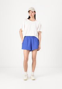 Biała, luźna koszulka, niebieskie szorty i kremowe sneakersy. Koszulka ma swobodny krój, a szorty są lekkie z elastycznym pasem.