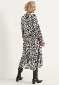 Langärmliges Blumenkleid in Creme mit navyblauen und hellblauen Mustern. Verfügt über ein gestuftes Design und wird mit schwarzen knielangen Stiefeln getragen.