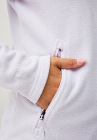 Jasnofioletowa polarowa kurtka z kieszenią zapinaną na zamek. Posiada fakturowaną powierzchnię oraz dopasowane mankiety rękawów z haftowanymi detalami.