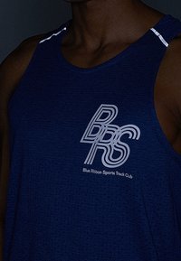 Osoba o ciemnej karnacji, ubrana w navy blue sportowy tank top z logo "BRS Blue Ribbon Sports Track Club" na piersi.
