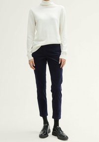 Vit polotröja med långa ärmar, parat med marinblå slim fit-byxor och svarta snörskor, som visar upp släta texturer och en åtsittande design.