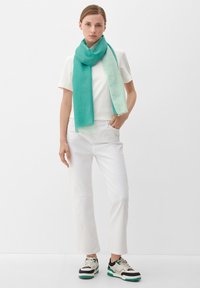 Écharpe dégradée turquoise et menthe en tissu léger, portée avec une chemise blanche et un pantalon blanc, présentant des bords effilochés.