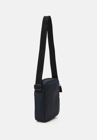 Borsa a tracolla blu navy realizzata in materiale liscio, dotata di una tracolla nera regolabile e una chiusura con zip dal design minimalista.