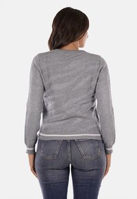 Maglione grigio lavorato a maglia con maniche lunghe, caratterizzato da un design texturizzato e orli a coste. Indossato con jeans attillati, mostrando una vestibilità rilassata.