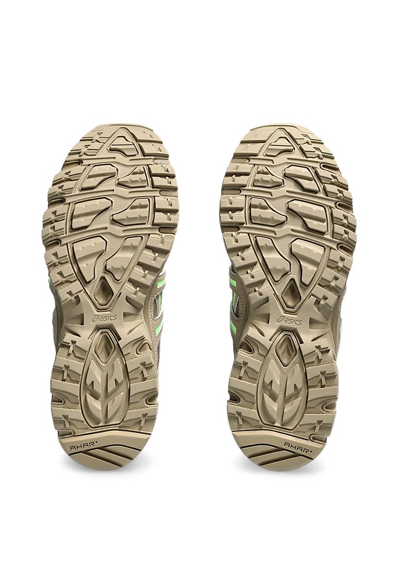 Zapatillas de trail running ligeras con una suela de goma beige texturizada, acentos verdes y un patrón de banda de rodadura multidireccional para mayor tracción.